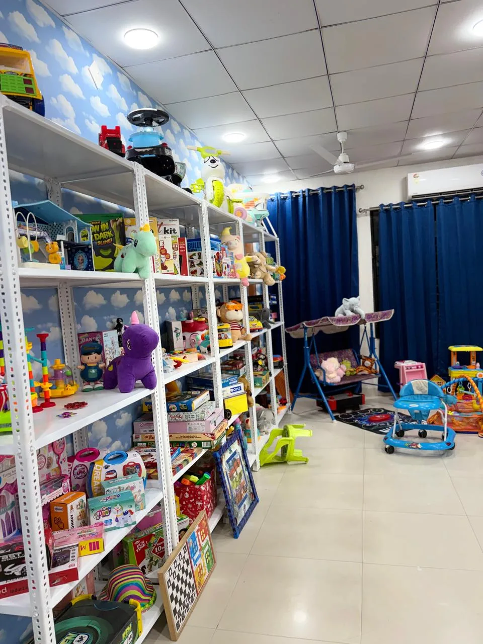 Shelves of board games and soft toys, with a baby walker and swing nearby